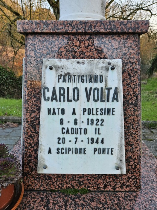 Cippo commemorativo dedicato al partigiano Carlo Volta, situato in un'area verde.