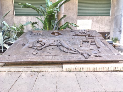 Monumento commemorativo con rilievi che evocano il tribunale di guerra nazista e le vittime del conflitto.