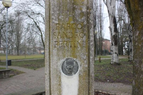 Monumento alla Resistenza con targa commemorativa, immerso in un parco alberato. Atmosfera di riflessione e memoria.