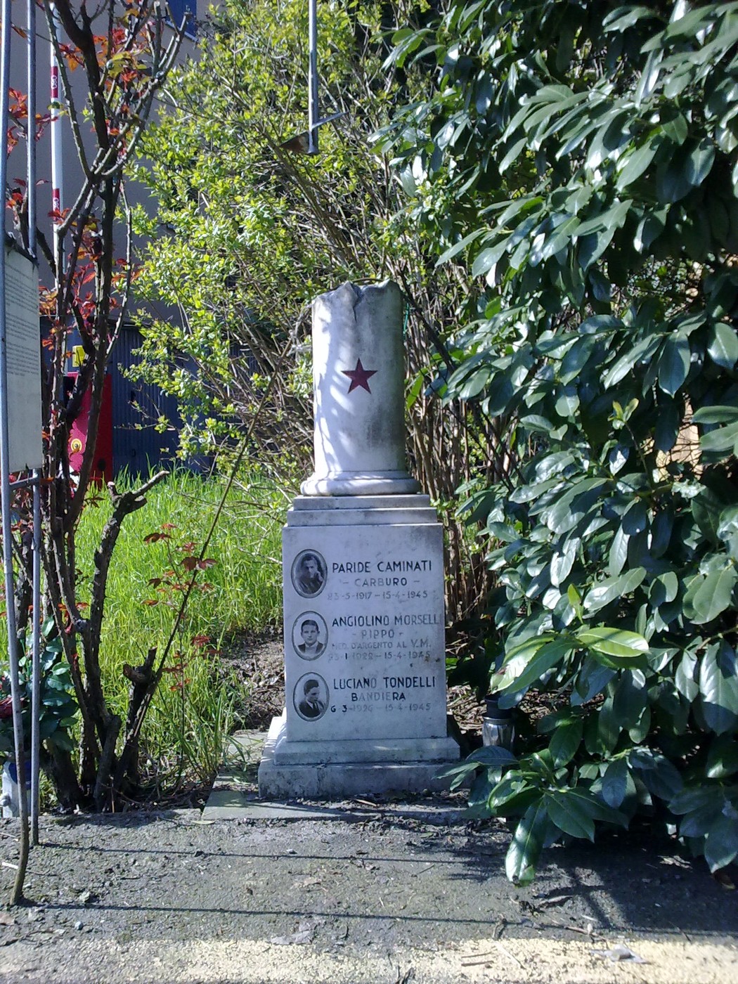 Cippo commemorativo dedicato a Carminati, Morselli e Tondelli, circondato da vegetazione.