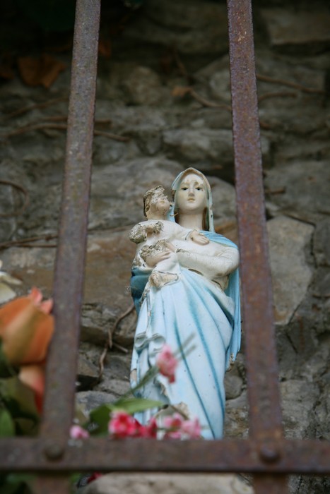 Statua della Madonna con Bambino nel tabernacolo di Falzano, incorniciata da una grata di ferro.