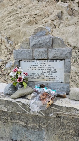 Monumento in memoria di Baldi e Cevenini, con fiori, situato in un'area naturale.