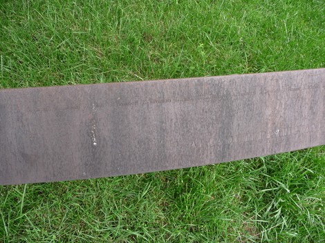 Monumento dedicato ai caduti partigiani, con superficie metallica e contesto erboso circostante.