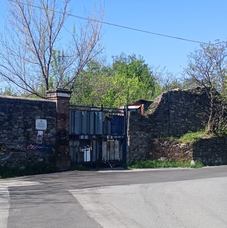 Porta di accesso con muro in pietra e vegetazione circostante, segno di storia e memoria.