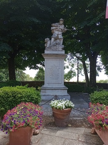 Monumento ai Caduti di Radicofani, con statue e fiori colorati in un contesto verdeggiante.
