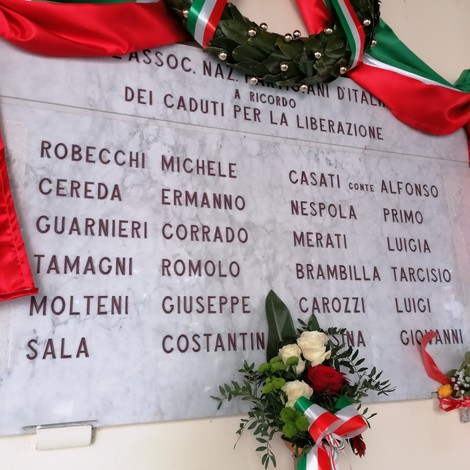 Lapide commemorativa dedicata ai caduti per la Liberazione, con decorazioni tricolori e fiori.