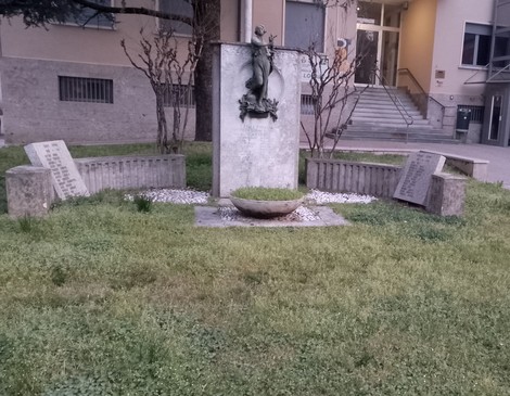 Monumento ai Caduti di Pozzuolo Martesana, circondato da piante e pietre, con un'imponente scultura centrale.