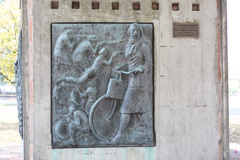 Monumento alla Resistenza con bassorilievo di figura femminile in bicicletta e scene di lotta.