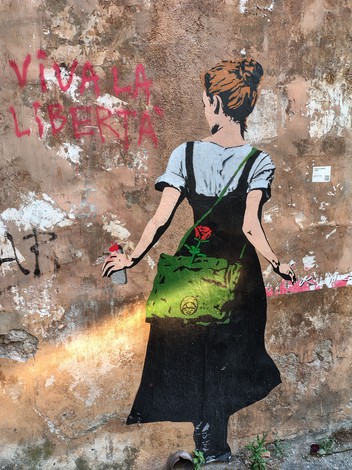 Murale che rappresenta una figura femminile con un fiore, simbolo di libertà, su un muro colorato.