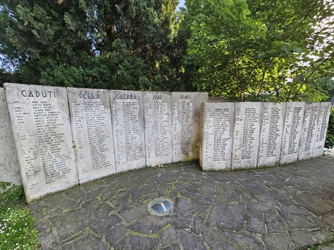 Monumento ai Caduti con elenchi di nomi incisi su blocchi di pietra, immerso in un contesto verde.