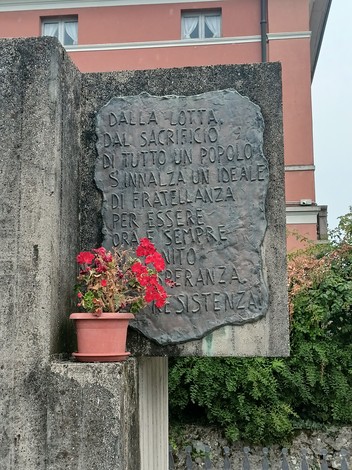 Monumento alla Resistenza con una placca commemorativa e fiori, simbolo di speranza e memoria storica.