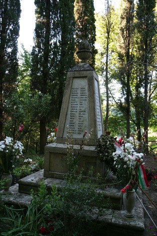 Monumento commemorativo dedicato alle vittime dell'eccidio di Guardistallo e Montescudaio, circondato da fiori.