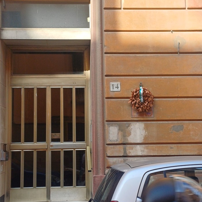 Portone d'ingresso al civico 14, con corona di alloro e piccola targa sulla parete accanto.