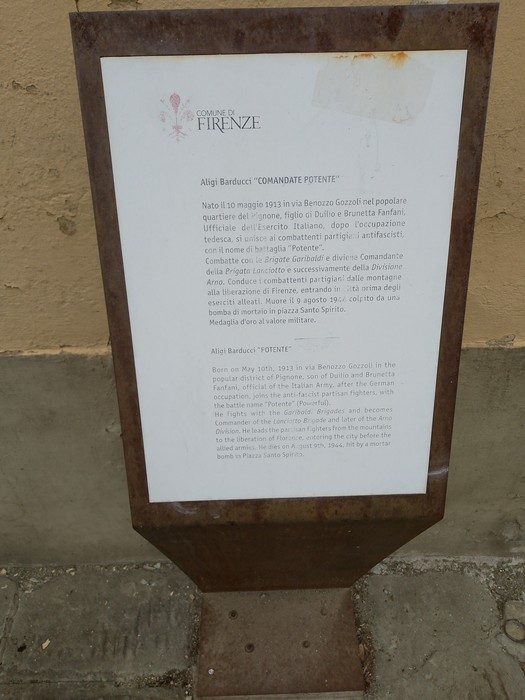Targa metallica con iscrizione dedicata a Aligi Barducci, montata su supporto arrugginito in strada.