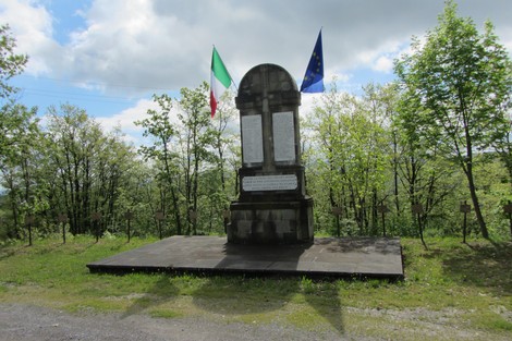 Monumento ai martiri dei Boschi di Ciano, circondato da alberi e bandiere italiana ed europea.