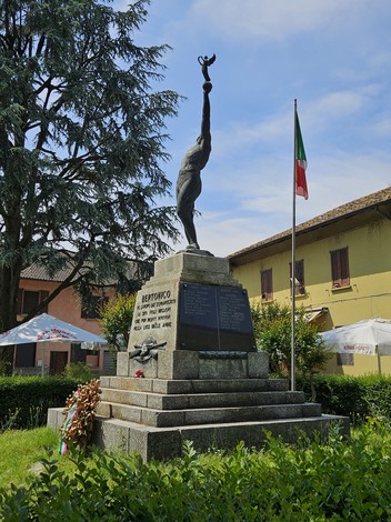 Monumento ai Caduti di Bertonico, con figura alata e bandiera italiana, immerso in un giardino curato.