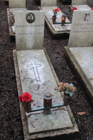 Decorazioni floreali e candele su una tomba nel cimitero dedicata ai caduti per la libertà, con incisioni su pietra.
