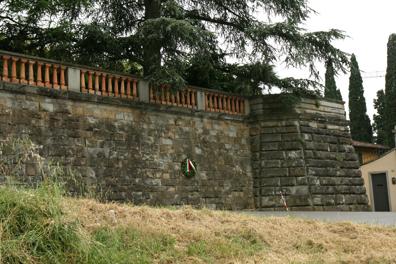Vecchia lapide a Giugni, incastonata in un muro storico circondato da alberi e piante.
