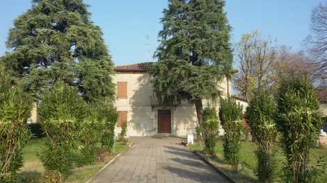 La fotografia mostra una casa circondata da alberi e piante, con un viale che conduce all'ingresso.