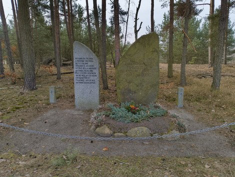 Monumento commemorativo circondato da alberi, dedicato al massacro di Treuenbrietzen, con pietre e un'aiuola.