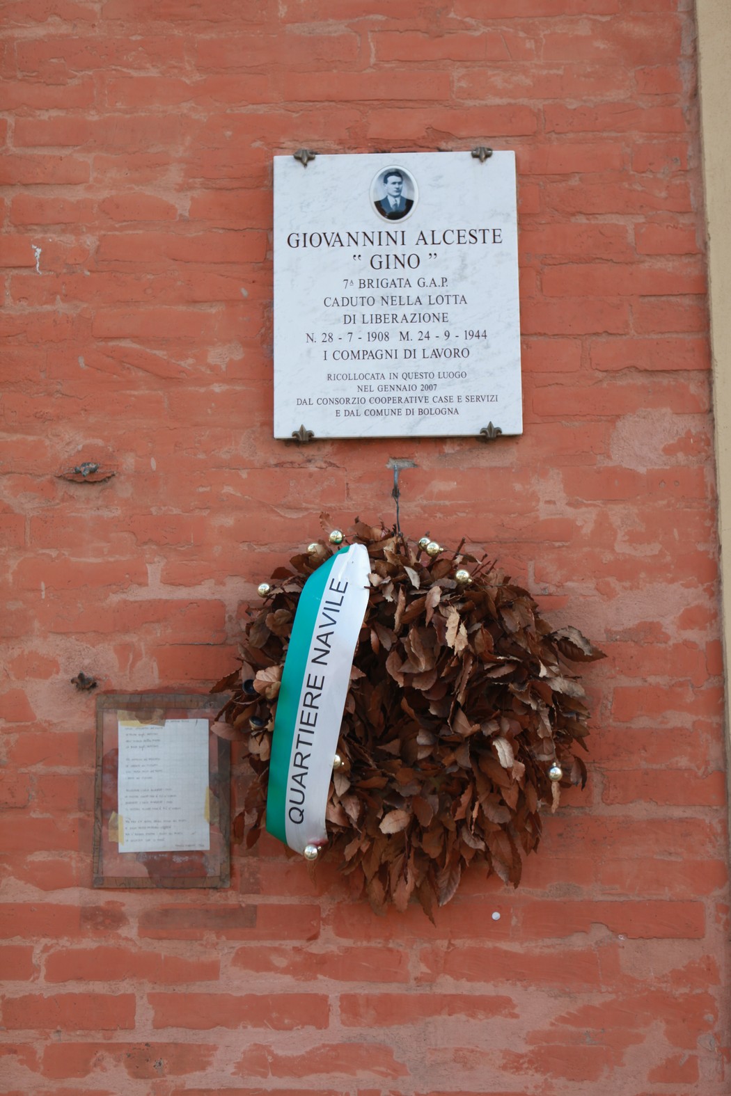 Lapide commemorativa dedicata a Giovannini Alceste, con una corona di alloro e un nastro del Quartiere Navile.