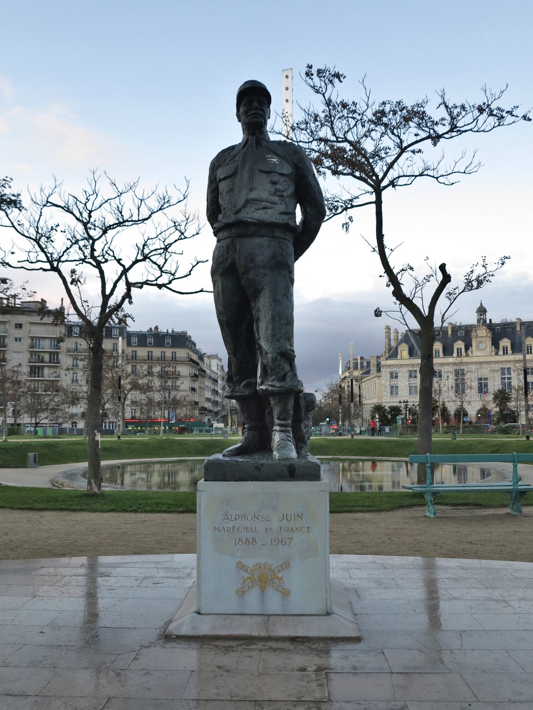 Statua di Adolphe Juin, generale francese, situata in un parco con alberi e edifici storici sullo sfondo.
