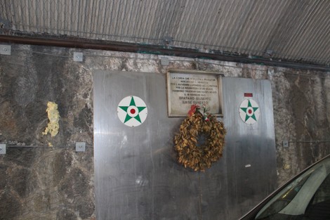 Lapide commemorativa dedicata a Spataro e Jursè, con corona di fiori, situata in un ambiente interrato.