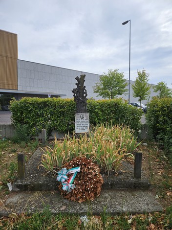 Cippo commemorativo a Valzania, circondato da piante, con una corona d'alloro ai piedi della stele.