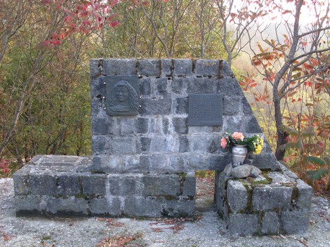 Monumento a Guidetti, un memoriale in pietra circondato dalla natura, con fiori e omaggi.