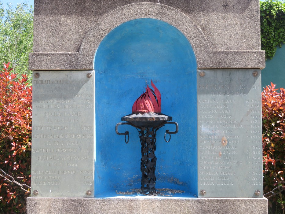 Monumento ai partigiani fucilati, con fiamma e targhe commemorative, simbolo di resistenza e memoria storica.