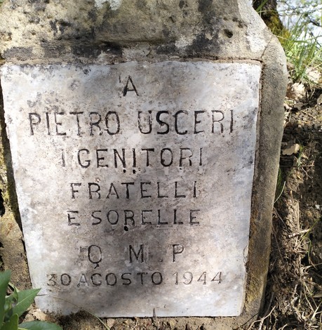 Cippo commemorativo dedicato a Pietro Uscieri, situato in un contesto naturale.