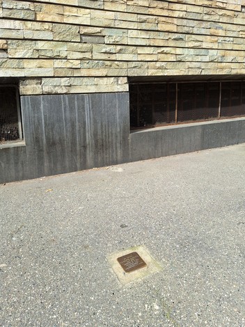Pietra d'inciampo a Ghiotti, collocata su un pavimento in cemento, vicino a un muro di pietra.