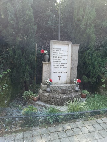 Monumento ai cinque martiri, circondato da alberi e fiori, simbolo di memoria e onore.