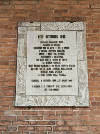 Lapide commemorativa che ricorda gli eventi dell'8 settembre 1943, su sfondo di mattoni rossi.