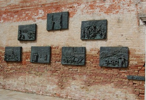 Il Monumento all'Olocausto presenta pannelli di bronzo incisi, raffiguranti scene commemorative su un muro di mattoni.