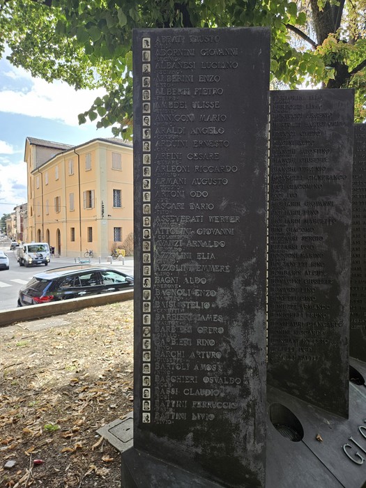 Monumento in lastre di pietra con iscrizioni, collocato sotto gli alberi lungo una strada.