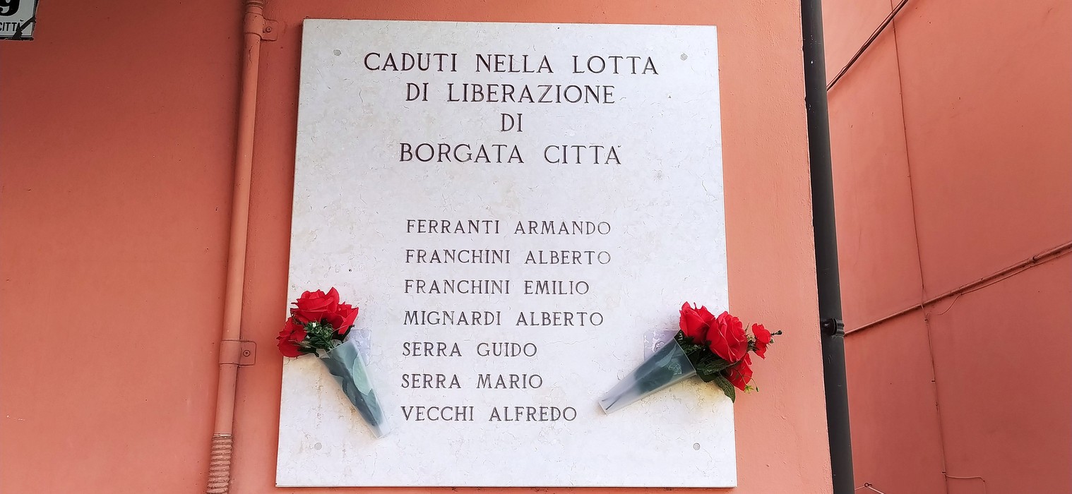 Lapide commemorativa con nomi dei caduti nella lotta di liberazione di Borgata Città, decorata con fiori.
