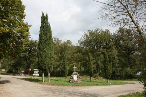 Monumento di Falzano immerso nel verde, con una croce e alberi circostanti lungo una strada tranquilla.