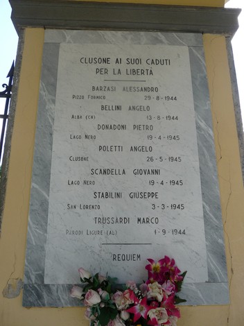 Lapide commemorativa ai caduti partigiani, con nomi incisi e fiori ai suoi piedi.