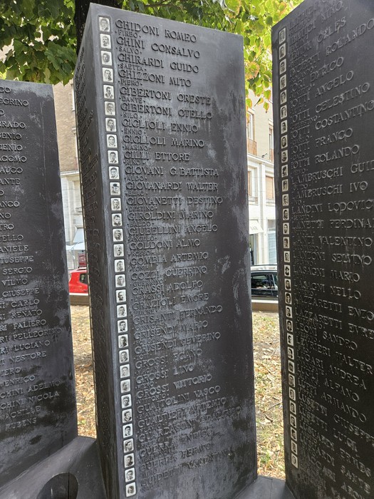 Monumento in lastre di pietra scura all'aperto, con iscrizioni e piccoli ritratti incisi.