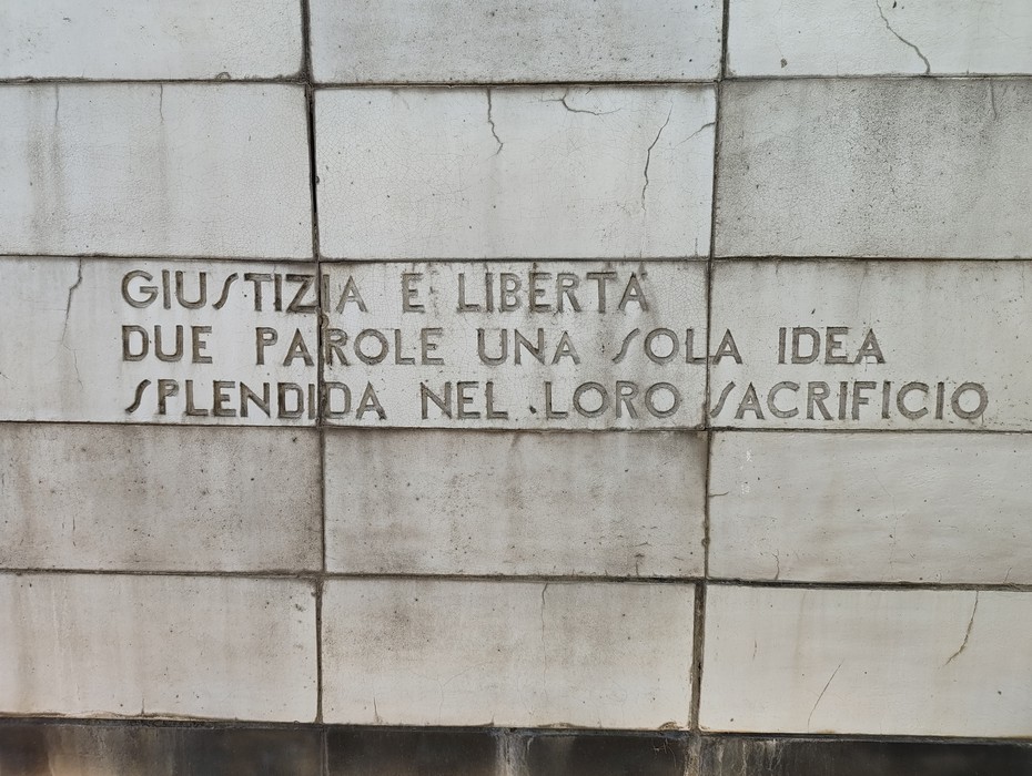 Lapide in pietra su parete a blocchi squadrati, con iscrizione a caratteri incisi.