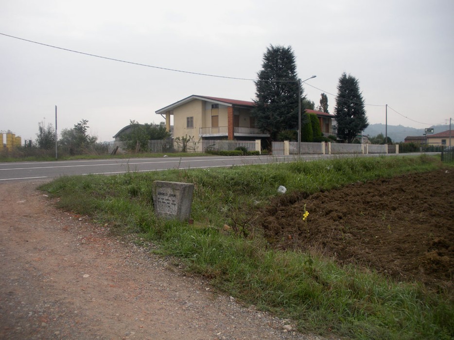 Lapide commemorativa a Zavattarelli, visibile lungo una strada in un'area rurale. Sullo sfondo, edifici e vegetazione.
