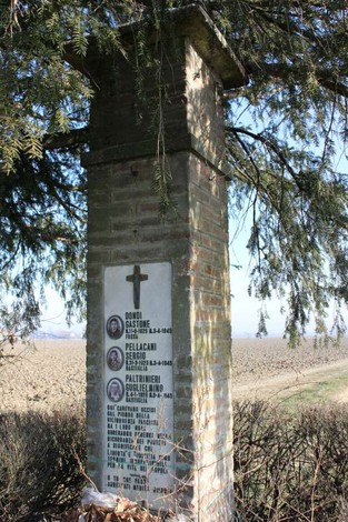 Cippo commemorativo dedicato a Dondi, Pellacani e Poltrinieri, situato tra la vegetazione e il paesaggio rurale.