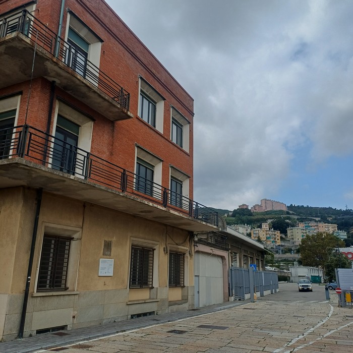 Edificio d'angolo in mattoni con targa commemorativa sulla facciata all'inizio di una via.