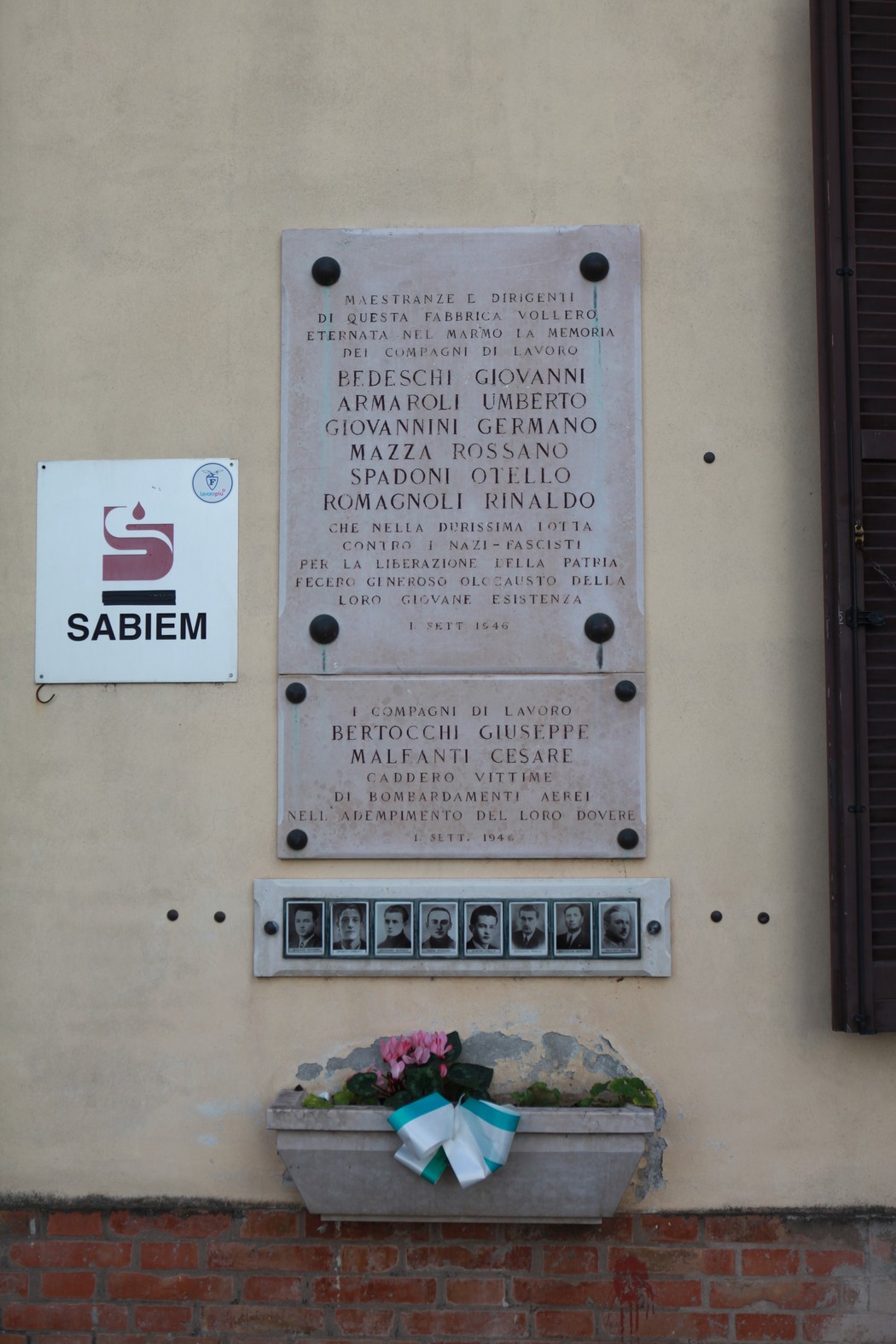 Lapide commemorativa in onore degli operai caduti, con epigrafe e fotografie in ricordo. Decorata con fiori.