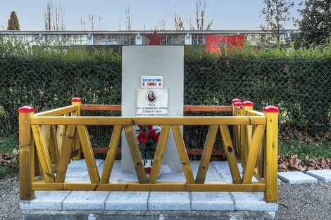 Cippo commemorativo dedicato a Benetti, circondato da una recinzione in legno e fiori.