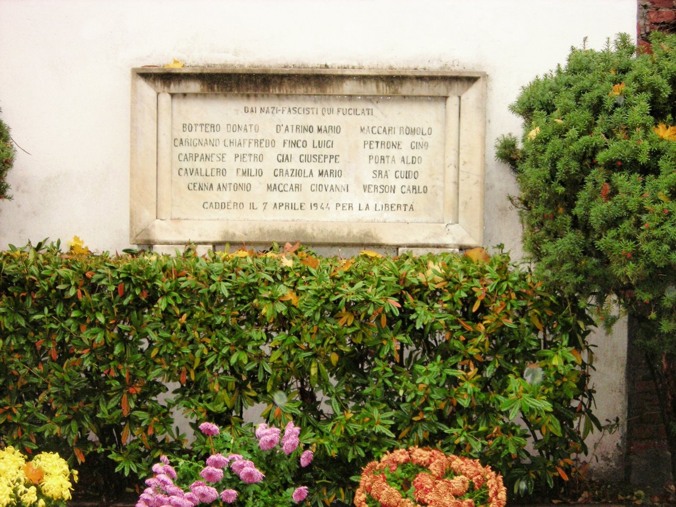 Lapide commemorativa dedicata ai fucilati di Caluso, situata in un contesto floreale.