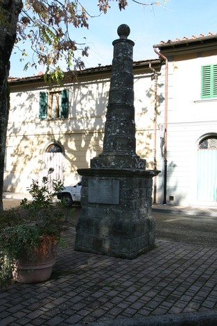 Monumento a Merendoni ed Ermini, obelisco stoneo situato in un contesto urbano con vegetazione circostante.