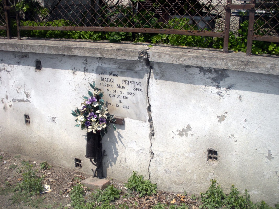 Lapide commemorativa dedicata a Peppino Maggi, con fiori e decorazioni sul muro.