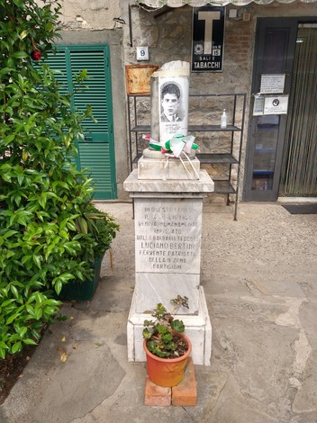 Cippo commemorativo dedicato a Luciano Bertini, partigiano, situato in un contesto urbano.